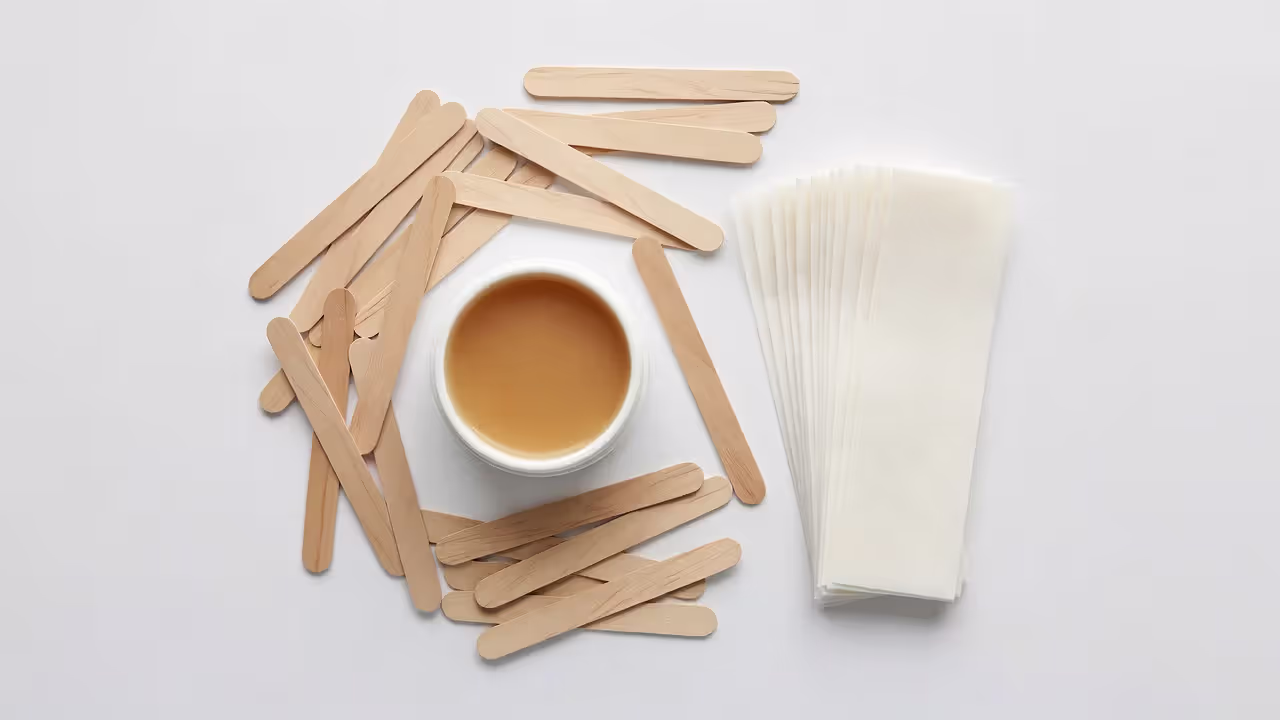 Waxing supplies including applicator sticks and wax strips on a clean surface